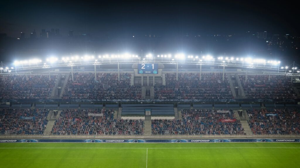 Football Soccer Stadium Championship Match, Scoreboard Screen Showing Score of 2:1. Crowd of Fans Cheering, Screaming, Having Fun. Sports Channel Television Advertising Concept. Wide Shot.